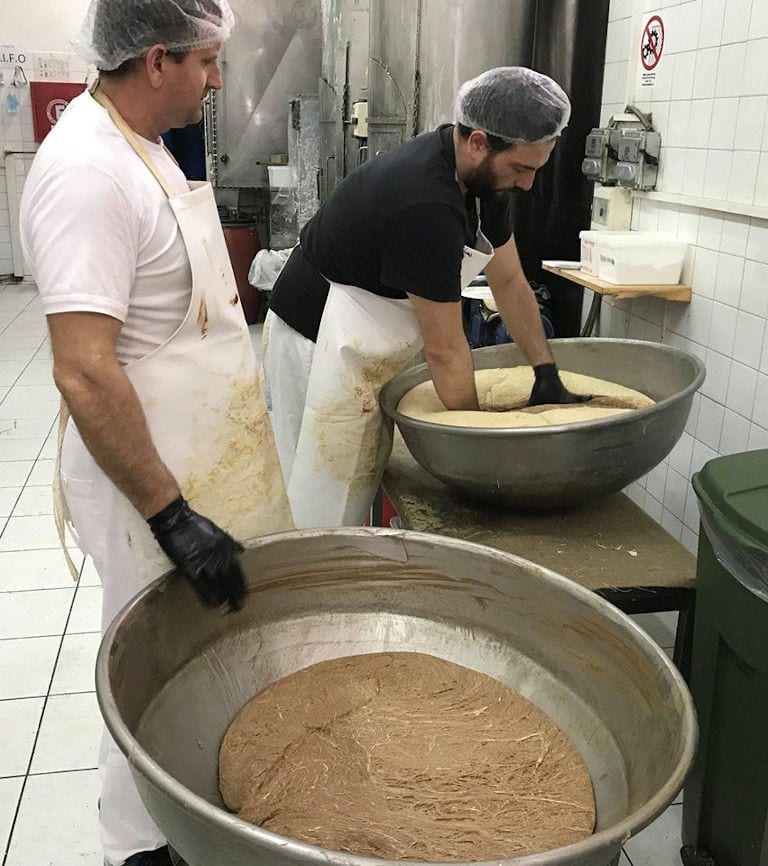 man with gloves mixing composition in a basin at 'M. Kosmidis' workshop with anothers worker waching him in the background